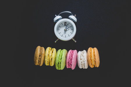 High detailed colorful macarons and white alarm clock on black background minimal conceptの写真素材