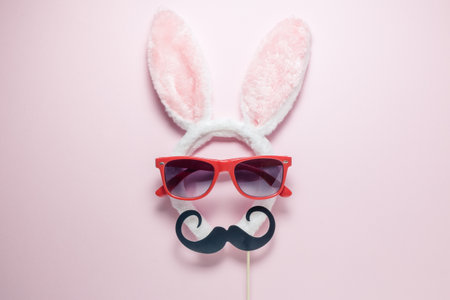 Flat lay minimal concept of abstract bunny with sunglasses and mustache on plain pastel pink...