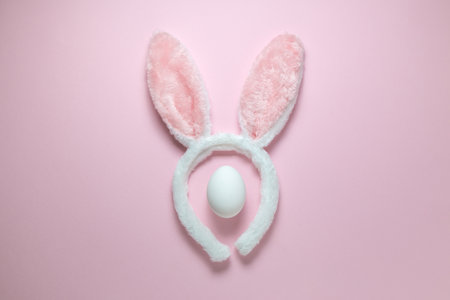 Flat lay of accessory costume bunny ears and white egg on plain pastel pink background. Easter minimal concept.の写真素材