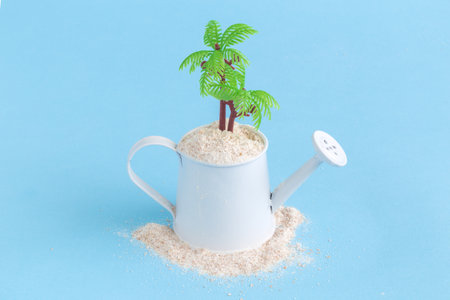 Small watering can full of sand with palm tree against blue pastel background. Summer vacation travel minimal concept.の写真素材