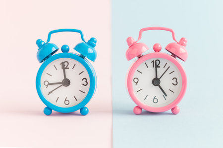Two small alarm clocks on pastel blue and pink background. Working hours minimal concept.の写真素材