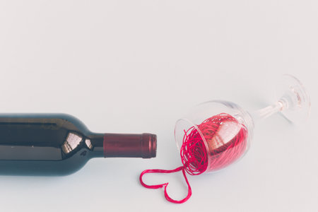 Bottle and crystal glass of wine made of red thread spilled in form of heart shape against blue background minimal creative concept.の写真素材