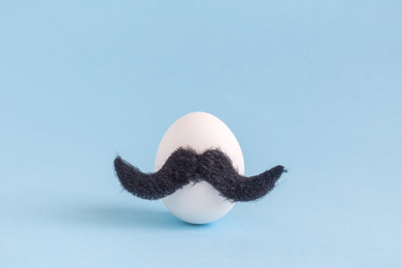 White egg with hipster mustache against pastel blue background. Minimal concept.の写真素材