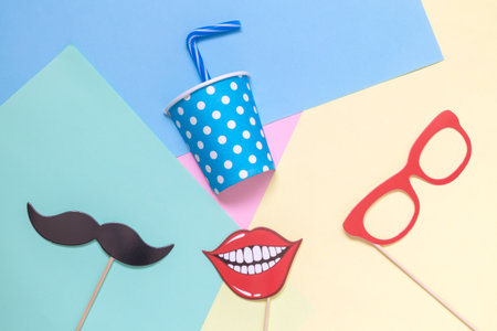 Flat lay of paper cup with drinking straw and photo booth props on multicolored pastel background minimal concept.の写真素材