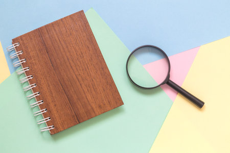 Magnifying glass and notebook against colorful pastel background flat lay minimal creative concept.の写真素材