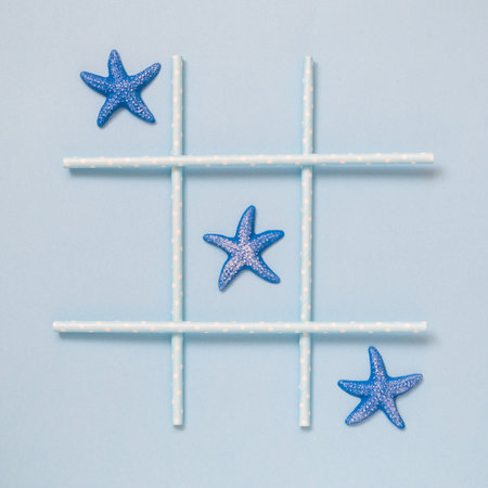 Tic tac toe made of sea stars and drinking straws on pastel blue background flat lay minimal conceptの写真素材