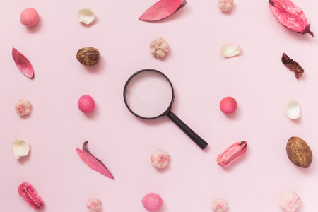 Dried flowers, leaves and plant parts pattern with magnifying glass on pastel rose background...