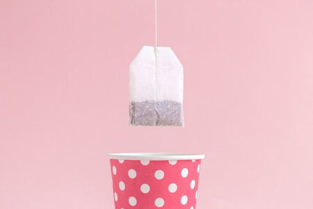 Dipping tea bag into paper cup polka design on pastel pink background minimal creative concept.