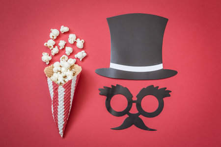 Flat lay of cone with popcorn and paper props on red background minimal movie theater concept