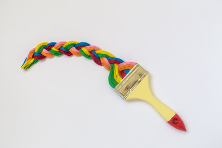 Paintbrush with long colorful strings braid isolated on white background minimal creative concept.