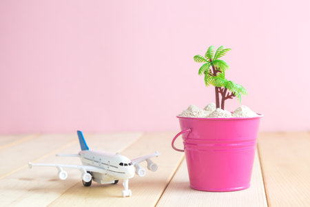 Airplane model toy and bucket full of sand with palm tree on table against pastel pink background minimal travel concept. Space for copy.の写真素材