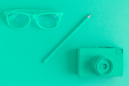 Flat lay of eyeglasses, pencil and retro film photo camera. Green colored background concept.の写真素材