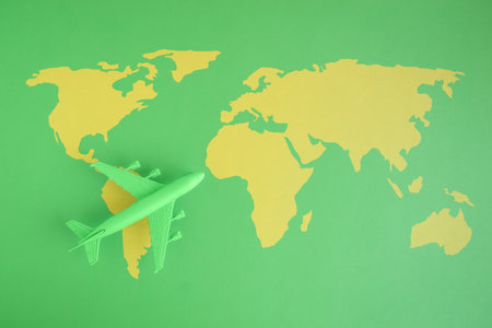 Flat lay of miniature toy airplane on green background with world map minimal trip and travel creative concepts.の写真素材