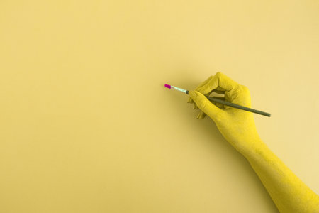 Female hand holding paintbrush. Yellow color minimal creative concept. Space for copy.