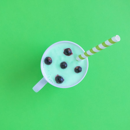 Flat lay of smoothie with blueberries and drinking straw against pastel green background minimal creative concept.の写真素材