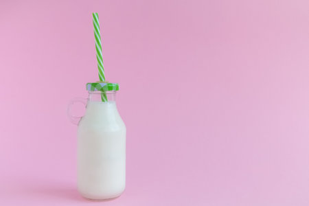 Small bottle of milk with drinking straw against pastel pink background minimal concept. Space for copy.の写真素材