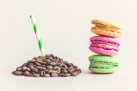 Pile of coffee beans with drinking straw and colorful macaroons on pastel pink background.の写真素材
