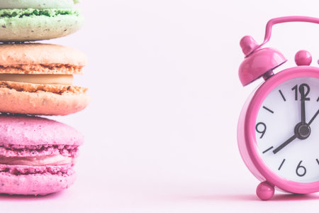 Colorful macaroons and small alarm clock on pastel pink background minimal creative concept. Space for copy.の写真素材