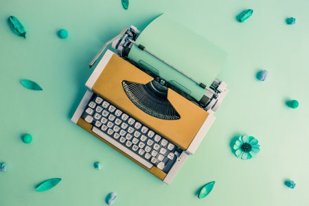 Flat lay of yellow retro typewriter against green flower pattern background minimal creative concept.の写真素材
