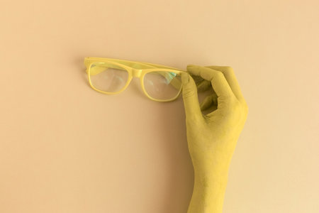 Female hand holding eyeglasses. Yellow colored minimal creative concept.の写真素材