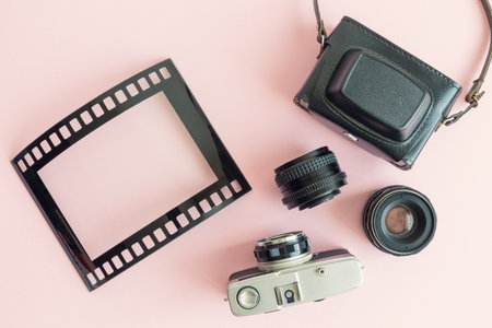 Flat lay of retro analog photo equipment and picture frame in form of film strip against pastel pink...