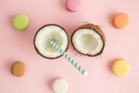 Coconut halves with drinking straw and macaroons on pastel pink background minimal creative concept.の写真素材