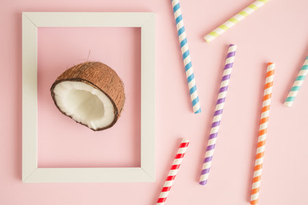Flat lay of framed coconut and colorful drinking straws against pastel pink background minimal summer tropical food and drink creative concept.の写真素材