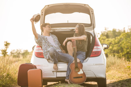 Modern couple taking a break and sitting on car hatchback. Travel and summer vacation concept.の写真素材