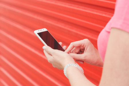 Close up of young woman using blank screen smart phone against red wall backgroundの写真素材