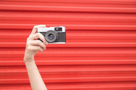 Close up of hand holding retro photo camera against red background. Space for copy.の写真素材