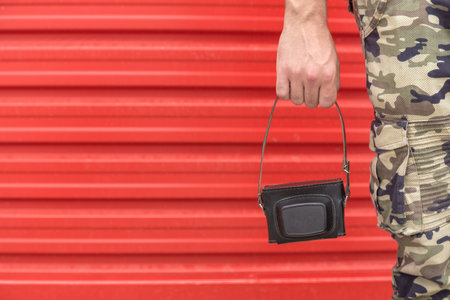 Close up of man hand holding photo camera case against red metal wall.