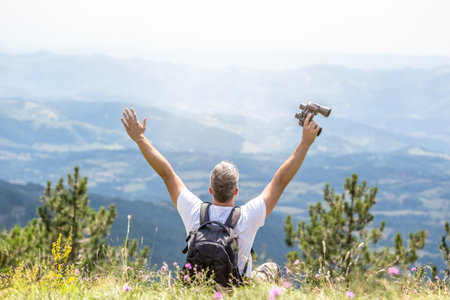 Backpacker sitting in the field on the top of the hill with hands up and enjoying the view
