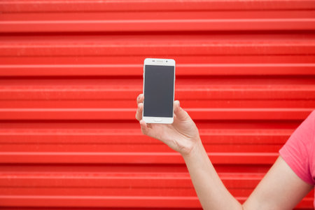 Close up of woman hand showing blank screen smartphone against red background.