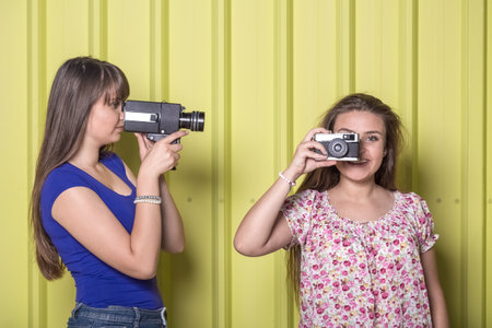 Young female friends holding retro video and photo cameras on yellow background.