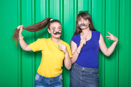 Portrait of two girls with mustache paper props on green background.の写真素材