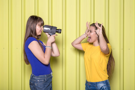 Two girls with retro analog video camera on yellow background.の写真素材