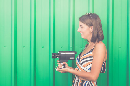 Hipster woman holding retro video film camera on green background.の写真素材