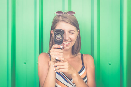 Portrait of a young smiling woman filming with retro camera isolated on green background.の写真素材