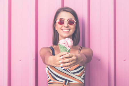 Cheerful woman with fruity ice cream in cone on pastel pink wall outdoors.の写真素材