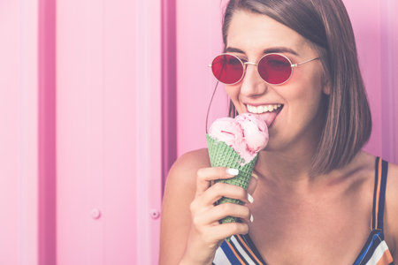Portrait of young urban woman with ice cream on pastel pink background.の写真素材