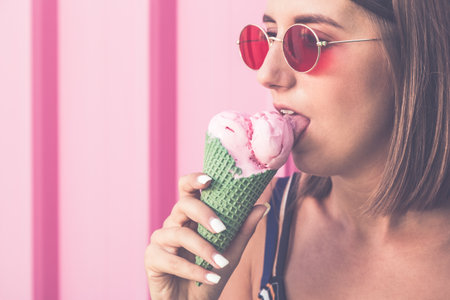 Portrait of young urban woman with ice cream on pastel pink background.