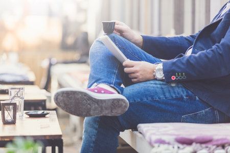 Close up of trendy man drinking coffee and using digital tablet while sitting in cafe outdoors.の写真素材