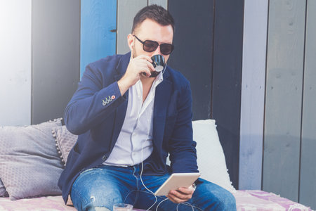 Urban guy drinking coffee and listen to music from his tablet device in cafe outdoors.の写真素材
