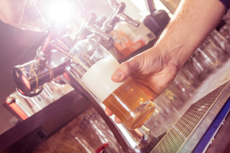 Close up of barman pouring lager beer in drinking glass.の写真素材