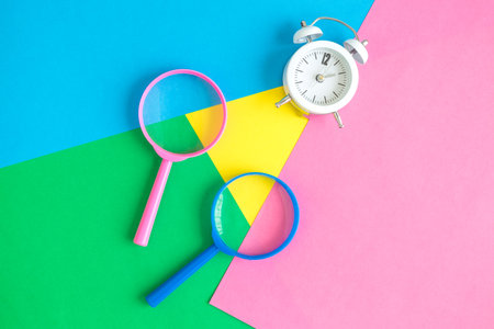 Rose and blue magnifying glasses with alarm clock against colorful pastel background flat lay minimal creative concept.の写真素材