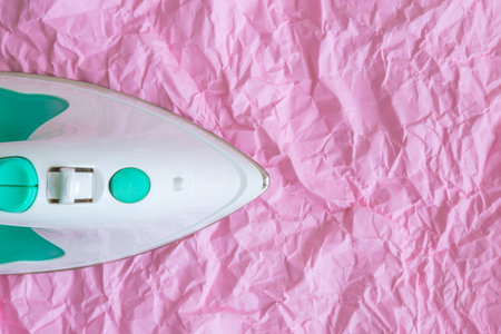 Top view of iron against pastel pink wrinkled paper minimal creative concept. Space for copy.の写真素材