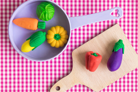 Top view of vegetable model toys on wooden cutting board and plastic pan on table minimal creative concept.の写真素材