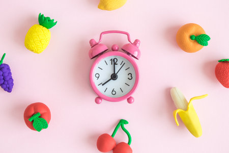 Flat lay of alarm clock and rubber fruit models on pastel pink background minimal creative concept.