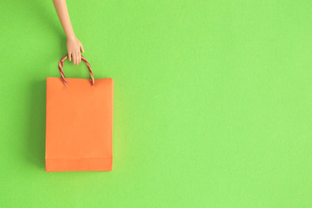 Doll hand holding shopping bag against pastel green background minimal creative concept.の写真素材
