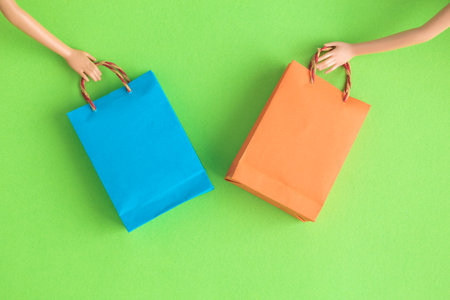Doll hands holding shopping bags against pastel green background minimal creative concept.の写真素材